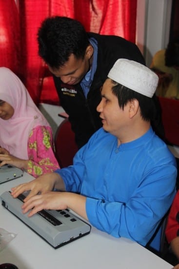 One of the E-Braille Research Team Personnel assists the People with Vision Disabilities (OKU) in learning of using the UTM invented E-Braille Panel (the grey color below) 